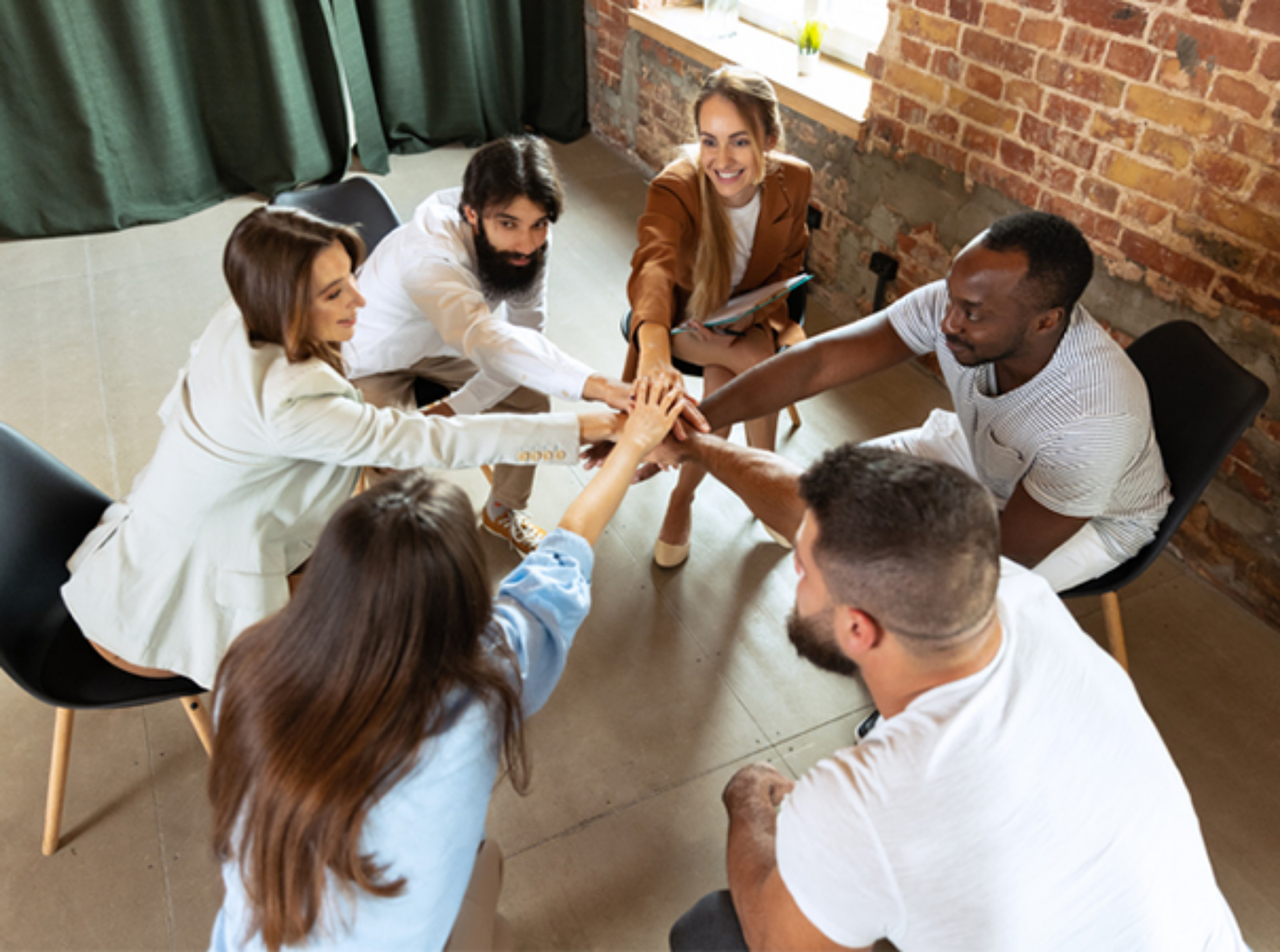 A diverse group of individuals seated at a table, enthusiastically raising their hands in a collaborative discussion.