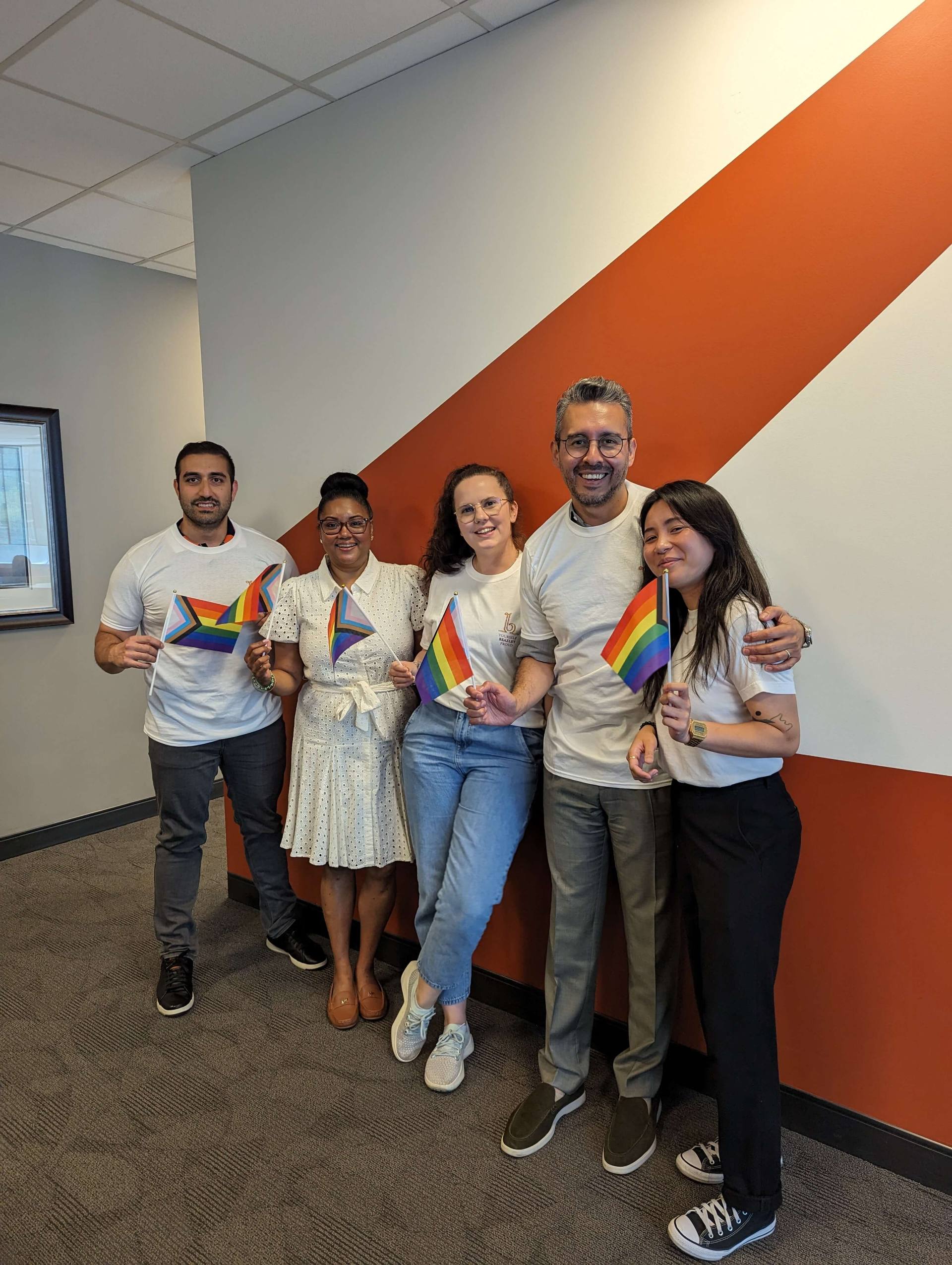 A team of proud colleagues standing together, smiling for a group photo in a well-lit office environment.