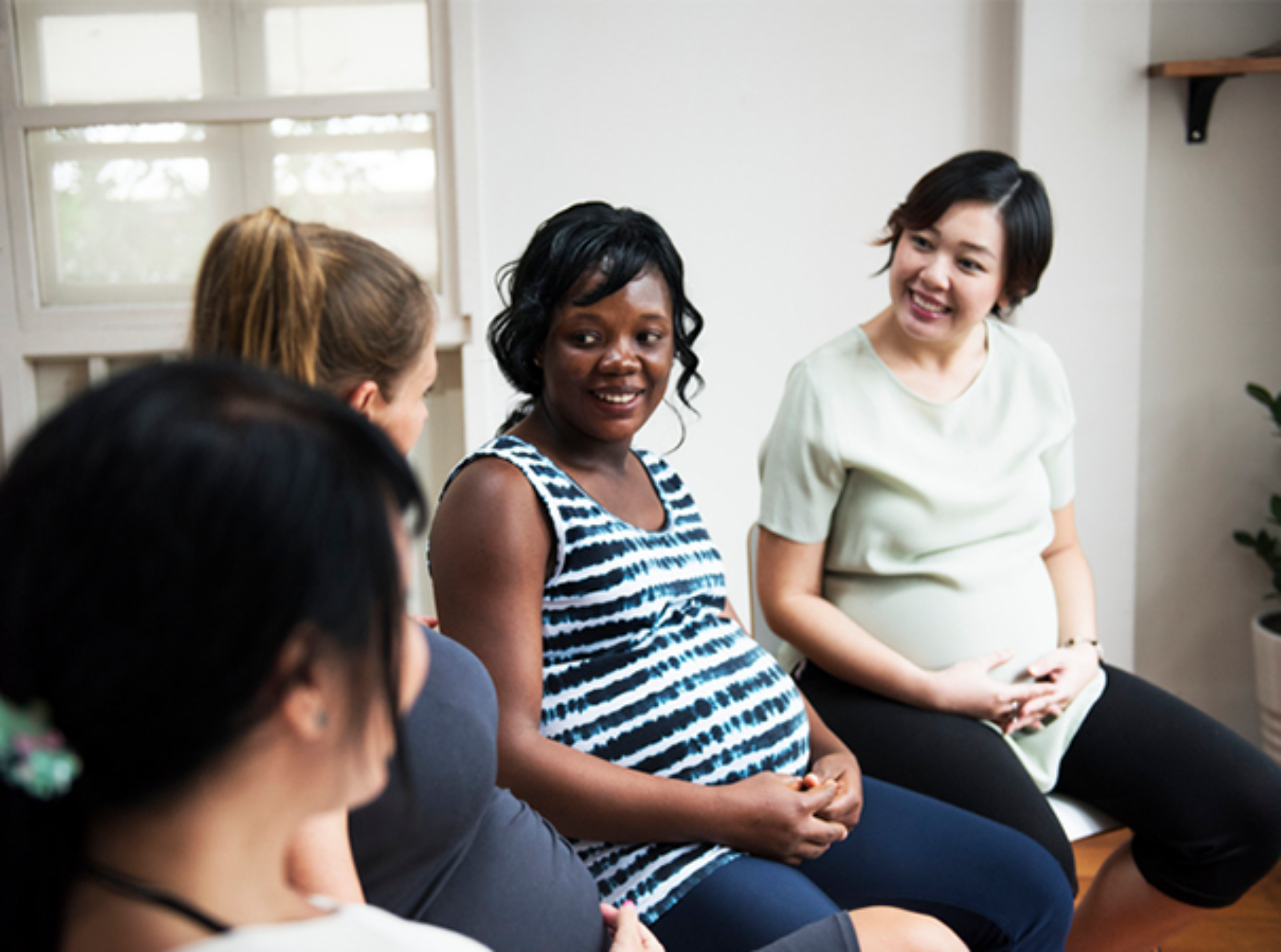 A diverse group of pregnant women seated together, engaged in conversation and enjoying each other's company.